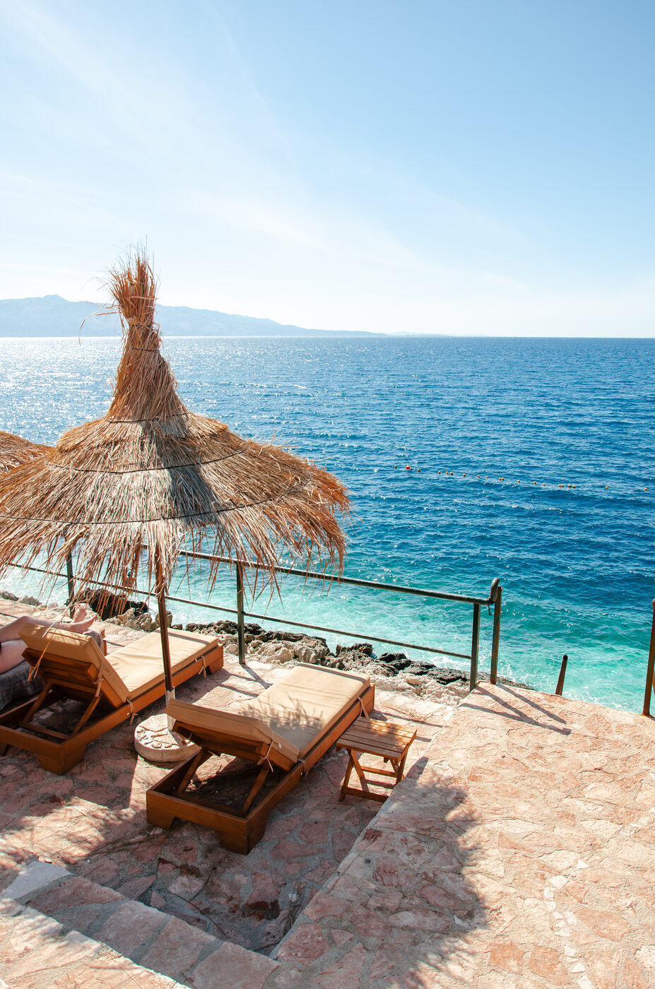 Thatched umbrella and wooden sun loungers over the Adriatic sea
